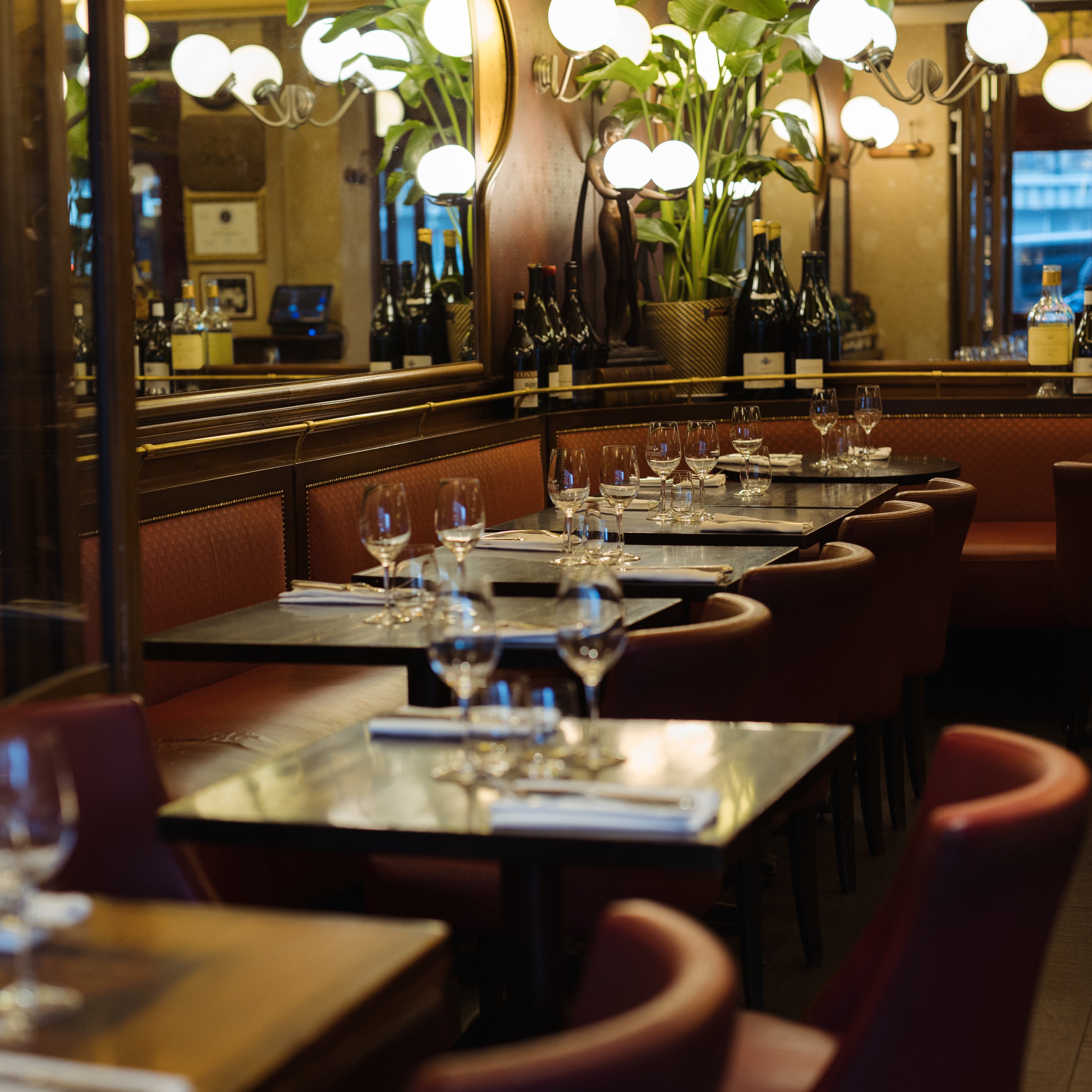 Elegant restaurant interior featuring tables set with glassware, plush red seating, and soft lighting from round lamps.