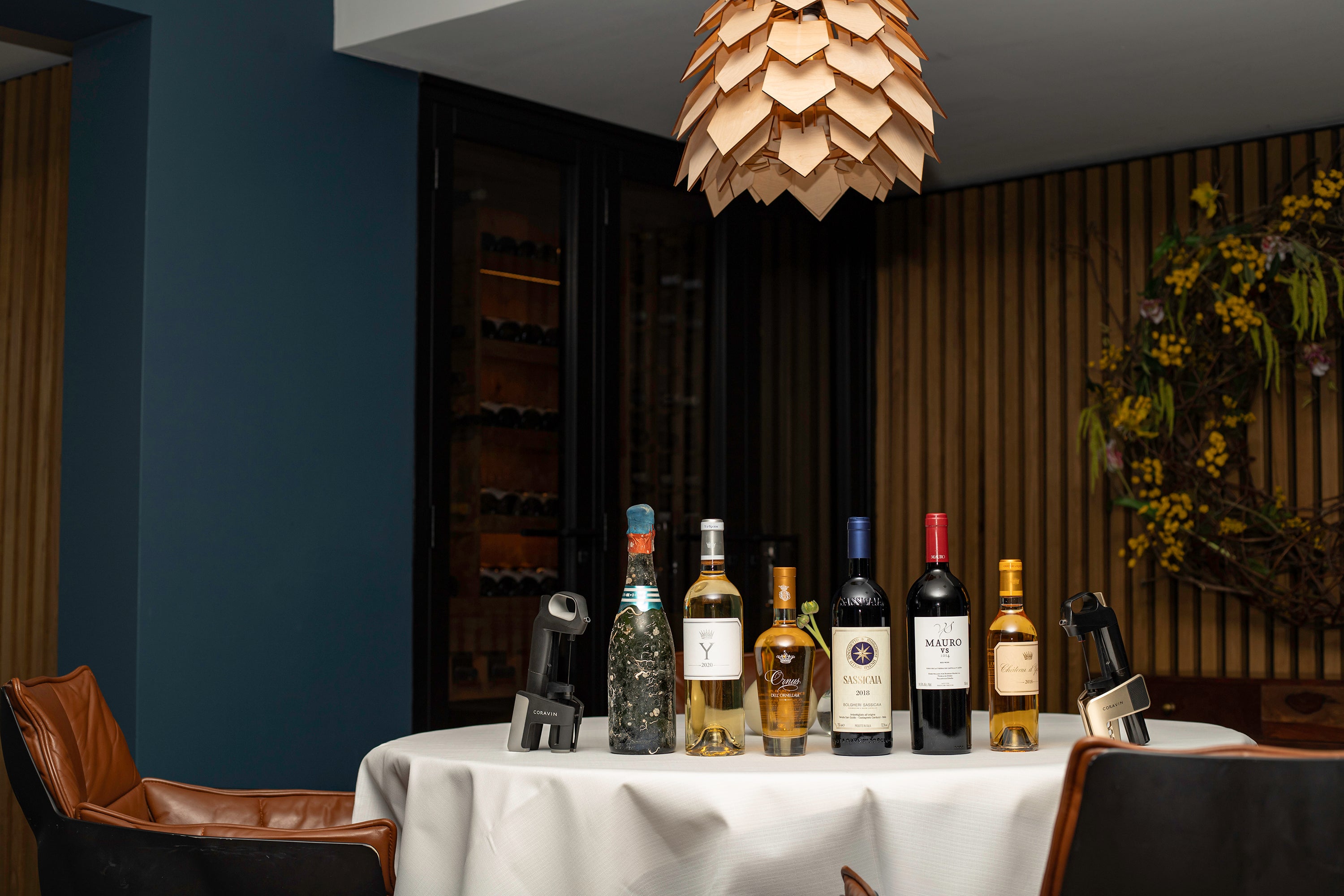 A selection of wine bottles displayed on a white table with a Cravin wine opener and wooden pendant lamp overhead.