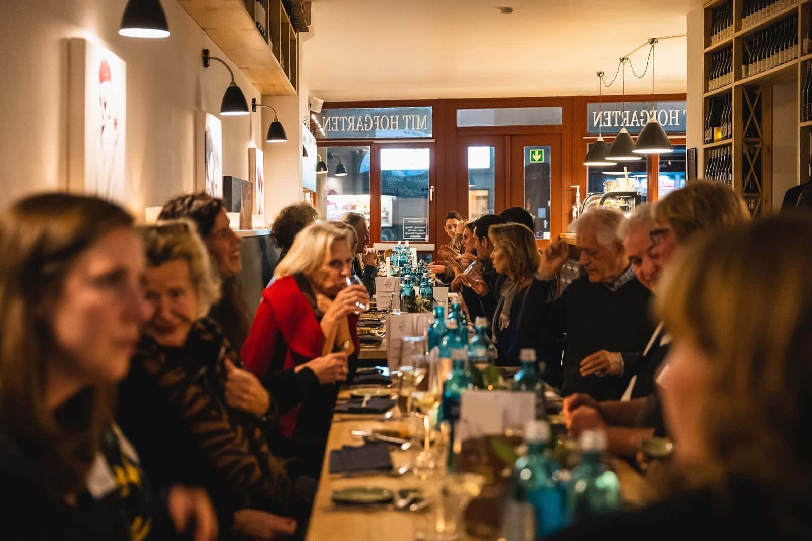 A long dining table filled with people enjoying a meal, featuring blue bottles and decorative place settings.