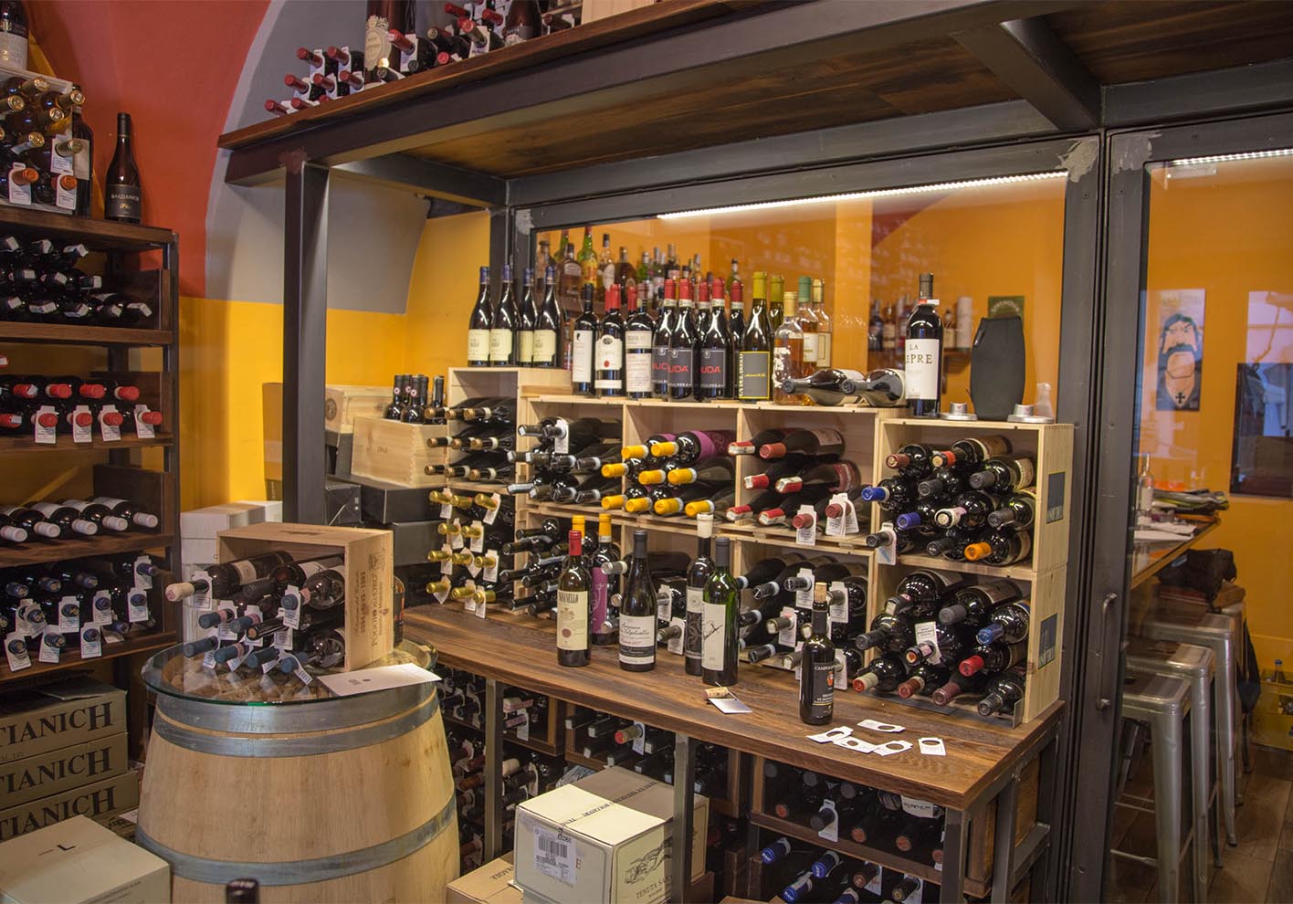 Wooden wine racks filled with various bottles, a barrel table, and wall shelves lined with wines in a store setting.