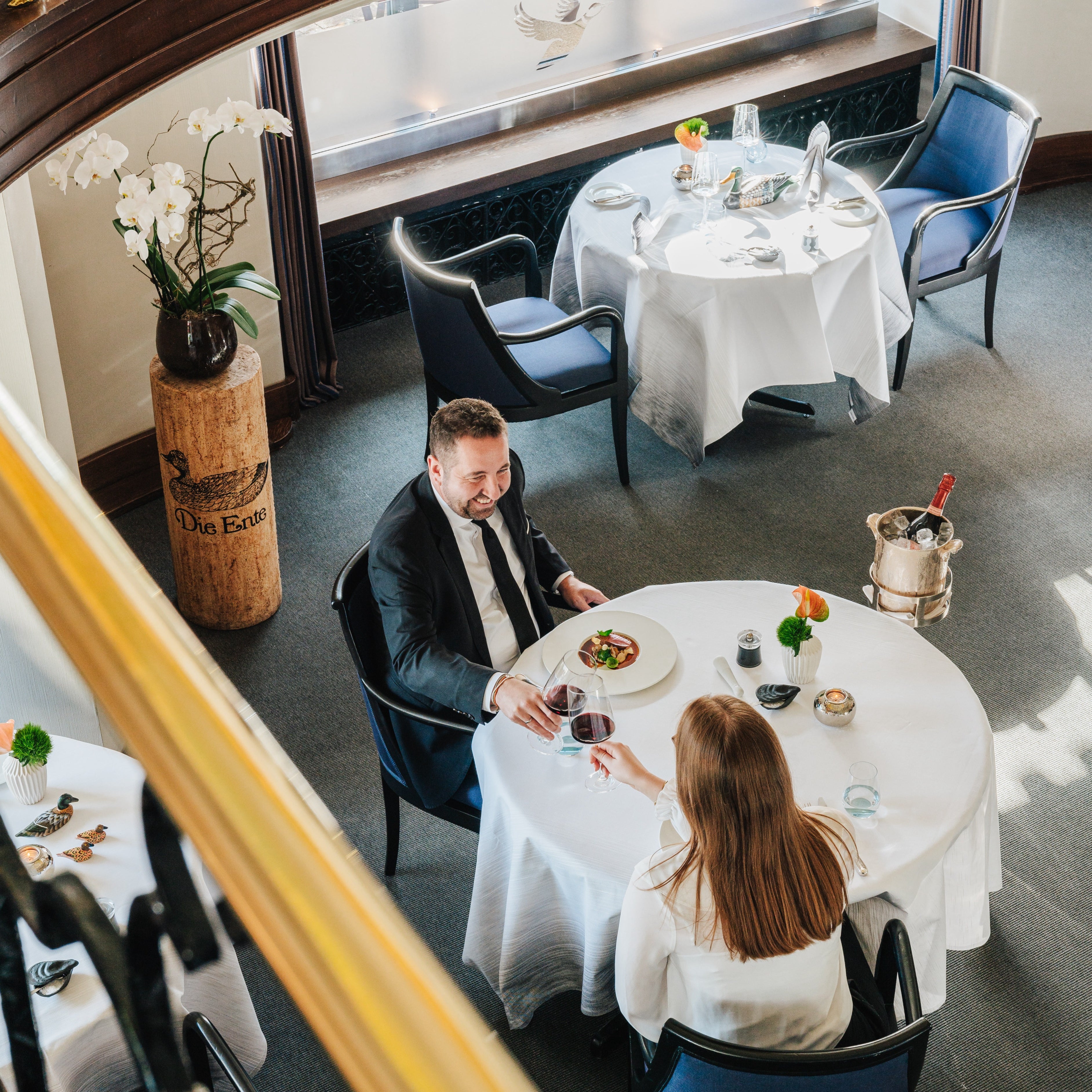 A couple enjoying a fine dining experience, toasting with glasses of red wine at a elegantly set table.