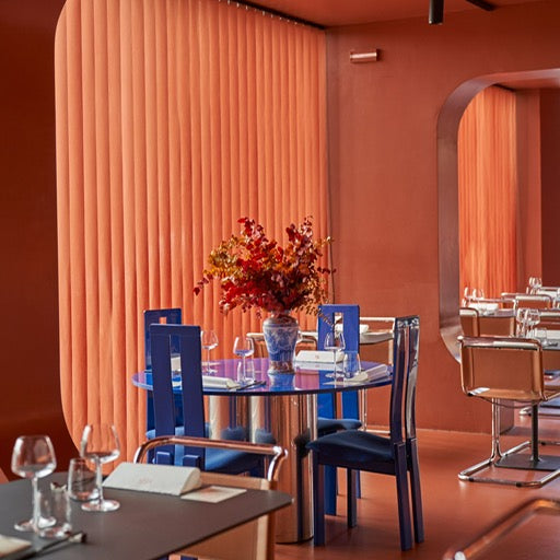 Brightly colored interior with orange walls, a round blue table, and a floral centerpiece, surrounded by modern seating.