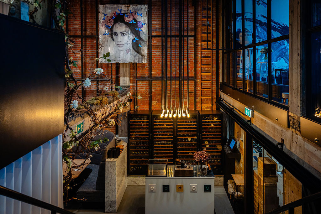 Modern restaurant interior featuring a large mural of a woman's face, a wine cellar, and cozy seating areas.