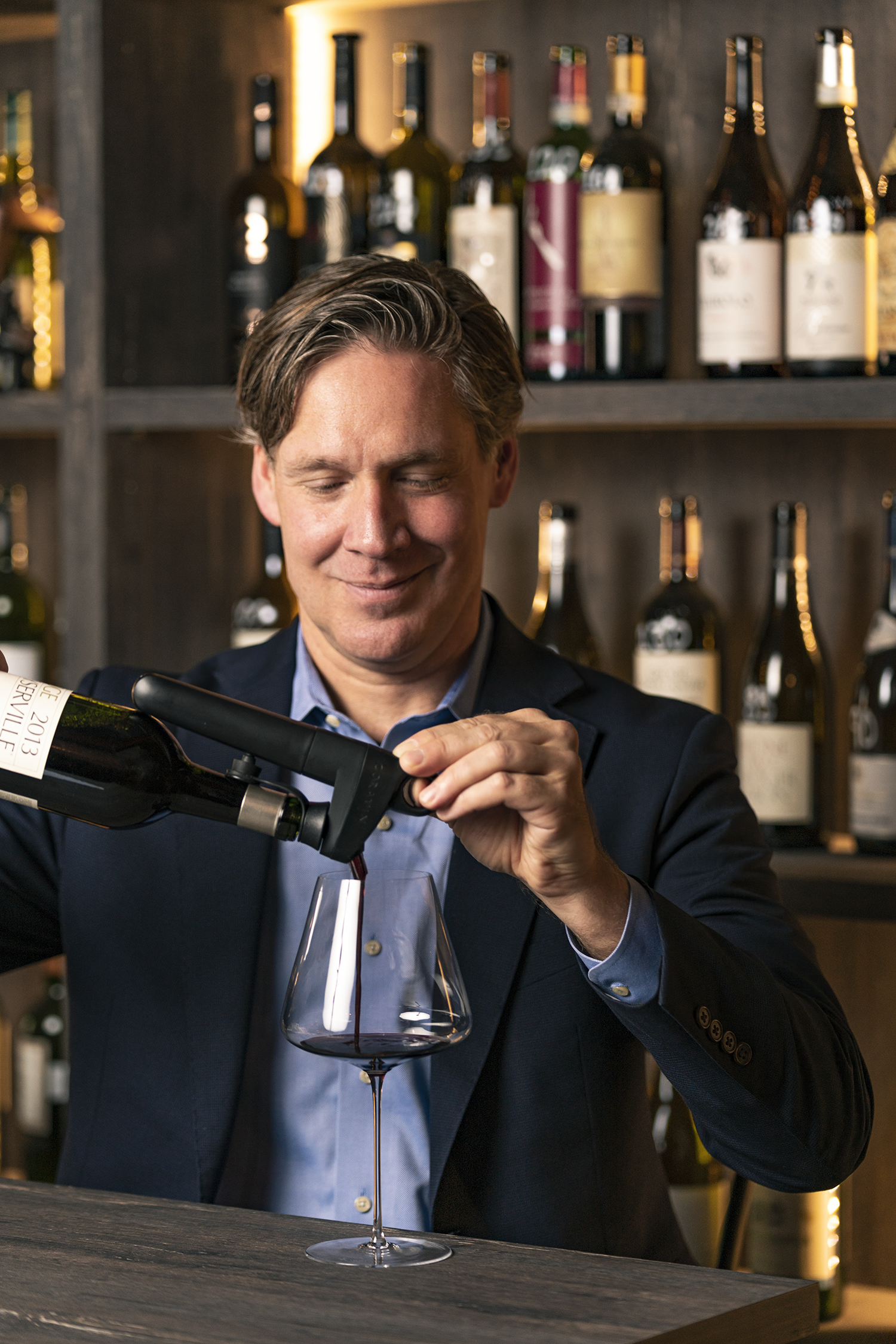 Man pouring wine with Coravin wine preservation system in front of wine bottles at a bar.