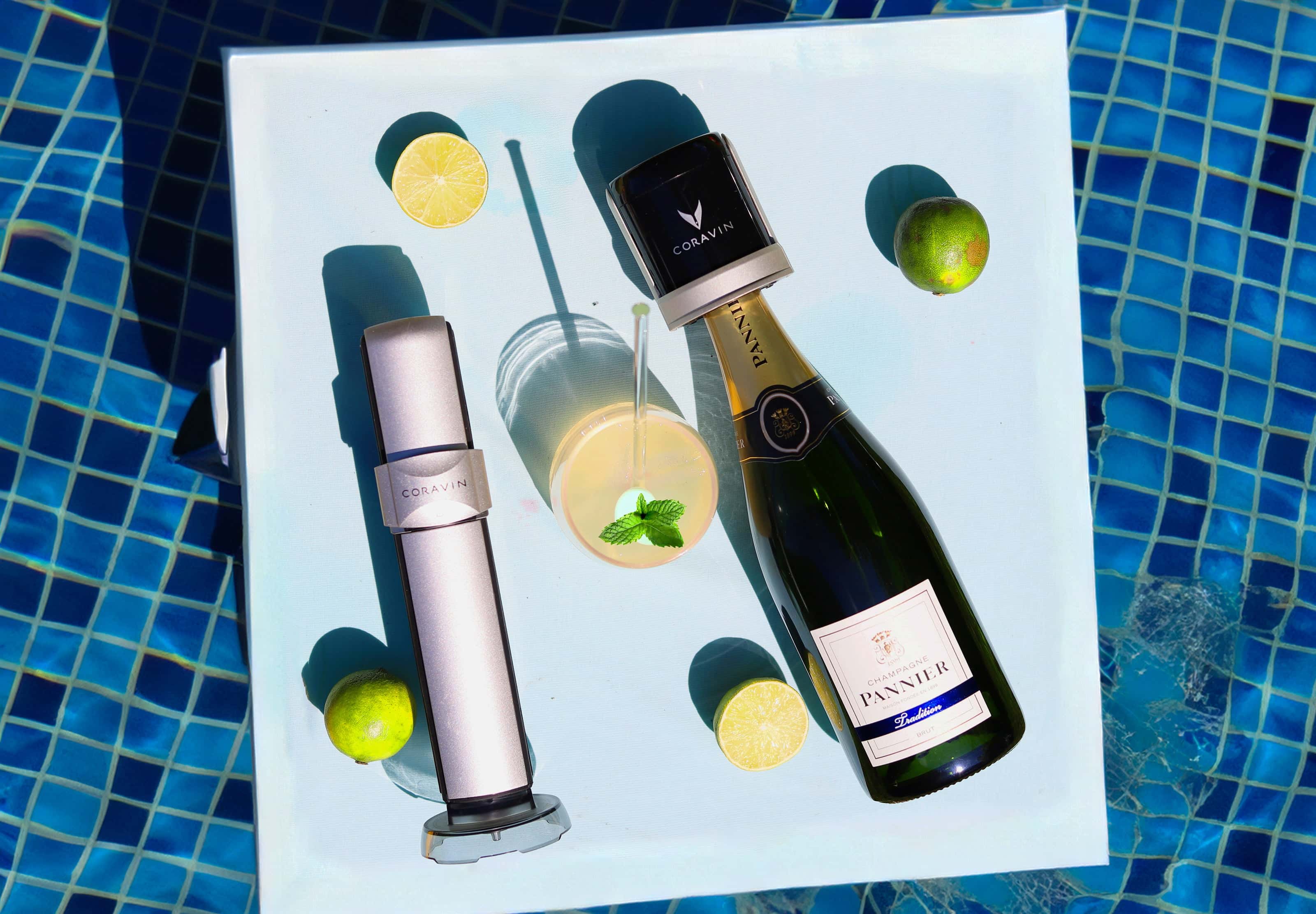 Coravin Sparkling system and Champagne Pannier bottle on a tray by the pool with a citrus cocktail, mint garnish, and fresh limes.
