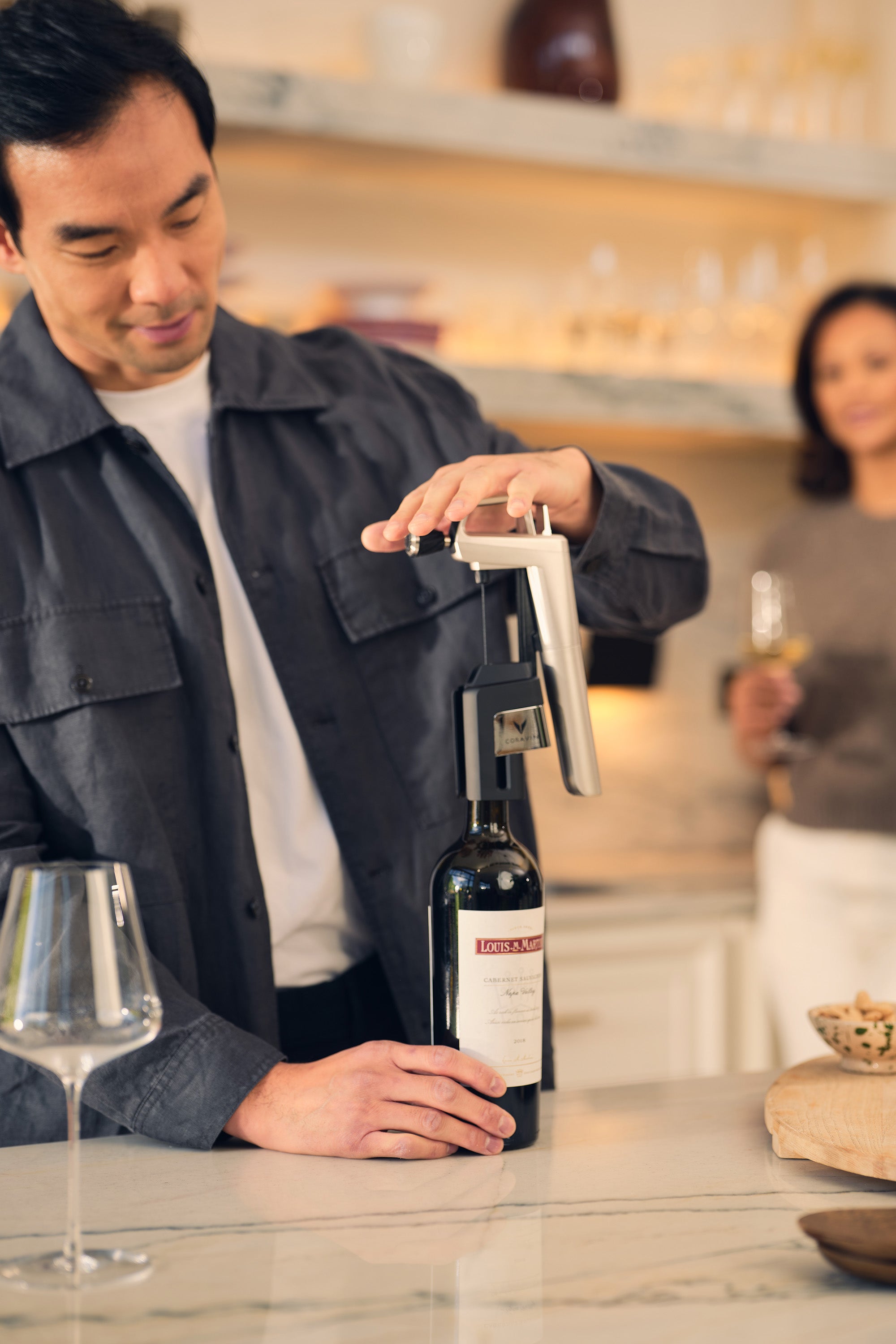 Man opening a bottle of wine with a Coravin in a kitchen setting.