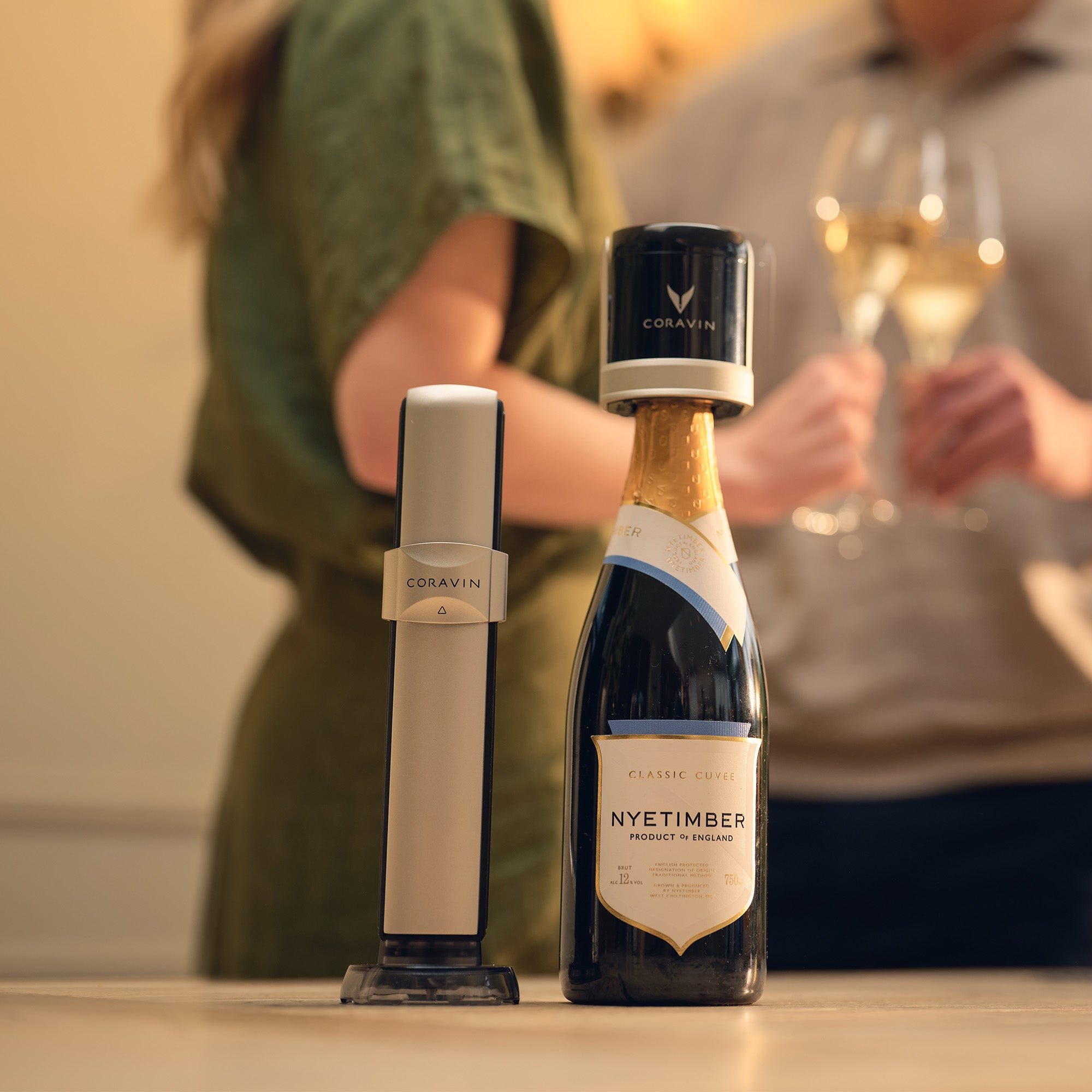 Bottle of Nyetimber wine with a Coravin wine opener on a table, with people in the background.