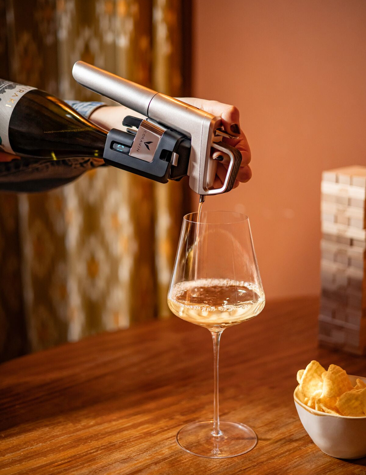 Person opening a bottle of wine with a coravin timeless pouring it into a glass on a wooden table with chips.