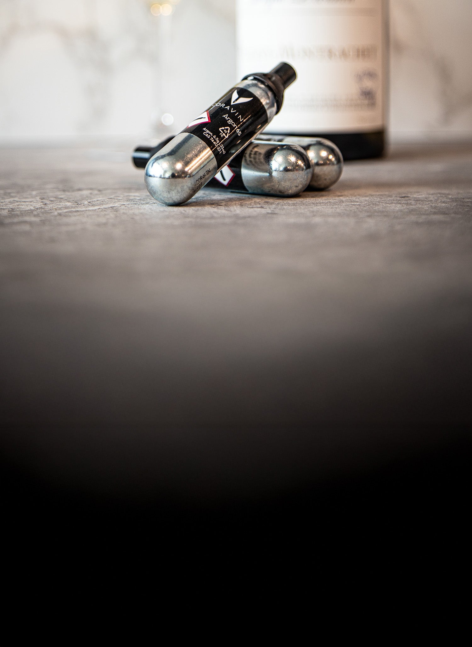 A black and silver Coravin wine preservation system with steel capsules on a textured surface, partially obscured by shadow.